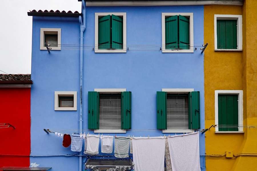 Façades de maisons aux couleurs peinture vives - bleu, jaune et rouge avec volets verts