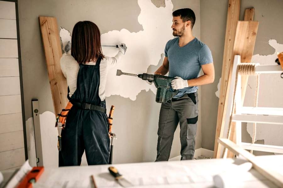 Couple réalisant des travaux rénovation intérieure avec perceuse dans salon en cours d'aménagement