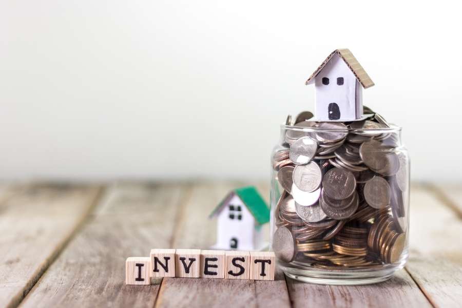 Un bocal en verre rempli de pièces de monnaie avec une petite maison posée dessus, symbolisant le besoin de diversifier ses investissements immobiliers.