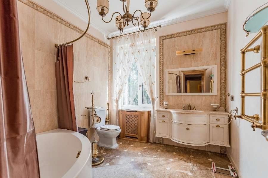 Une salle de bain vintage luxueuse avec des murs en marbre beige, un lustre et une baignoire ancienne.