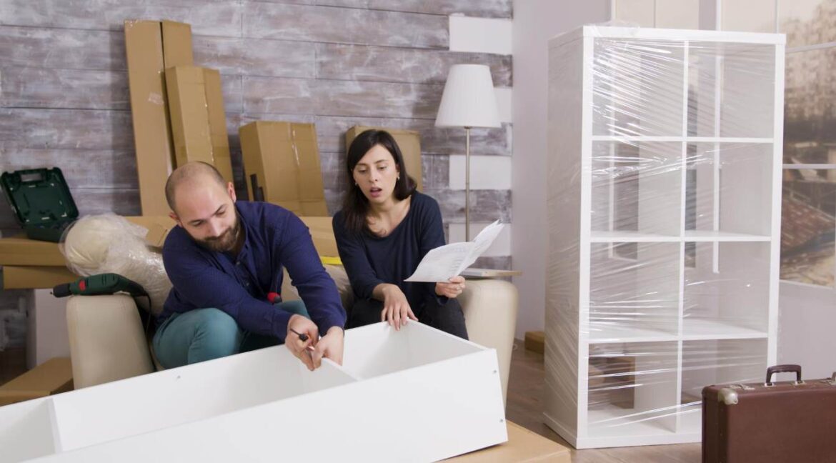 Un couple assemble un meuble en kit dans un salon entouré de cartons, soulignant l'importance de calculer le volume d’un déménagement avant l'arrivée.