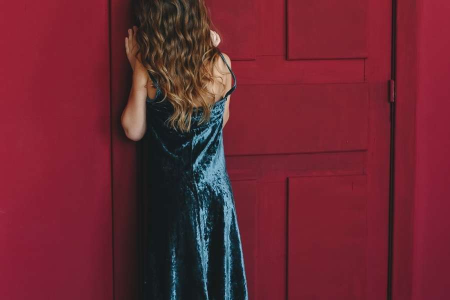 Une personne dépitée en robe bleue se tient devant une porte claquée de couleur rouge vif