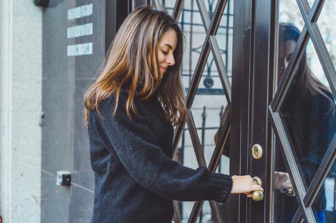 Une femme ouvre la porte vitrée d'un immeuble parisien, illustrant l'importance d'une installation soignée par un comparaison marque serrure fichet fichet fichet serrurier paris.